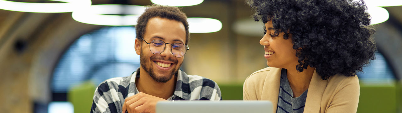Hombre con gafas y camisa de cuadros sonriendo junto a una mujer con cabello afro, frente a un portátil